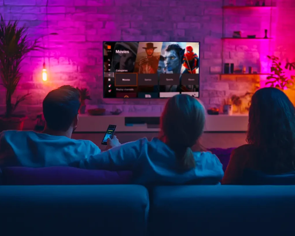 Une famille regarde la TV dans le canapé du salon dans une ambiance colorée