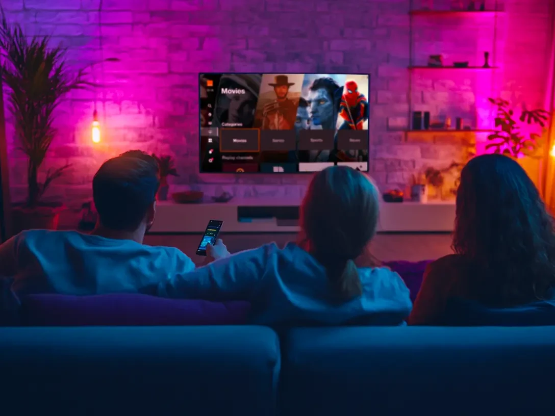 Une famille regarde la TV dans le canapé du salon dans une ambiance colorée
