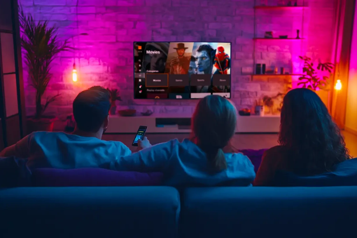 Une famille regarde la TV dans le canapé du salon dans une ambiance colorée