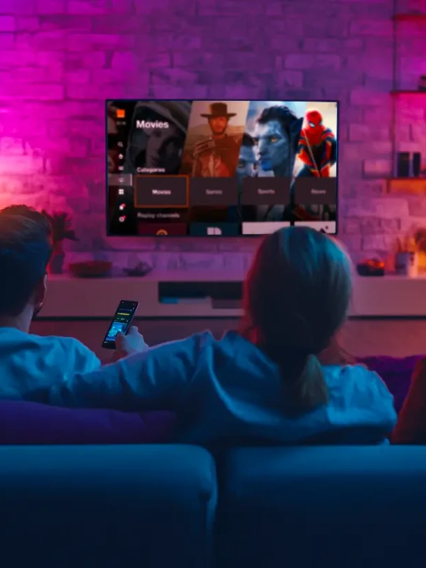 Une famille regarde la TV dans le canapé du salon dans une ambiance colorée