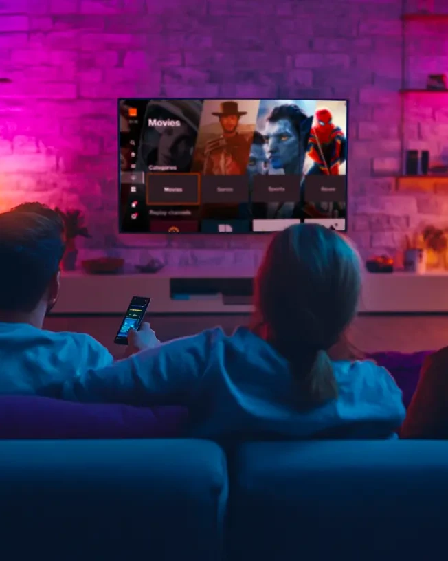 Une famille regarde la TV dans le canapé du salon dans une ambiance colorée