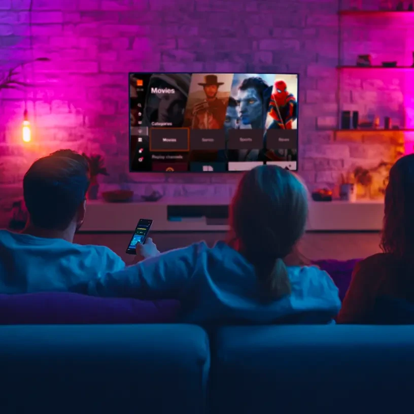 Une famille regarde la TV dans le canapé du salon dans une ambiance colorée